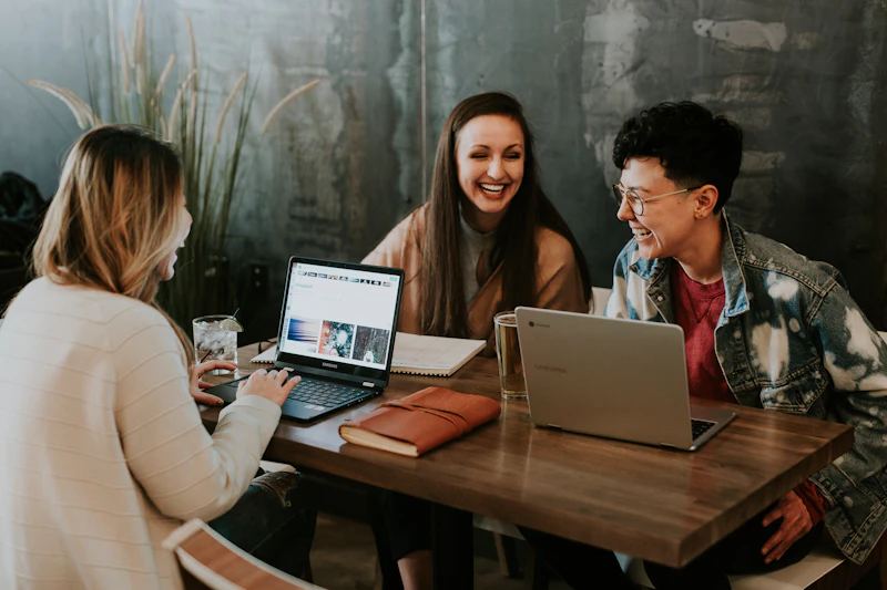 Três pessoas conversando e rindo em volta de uma mesa com notebooks
